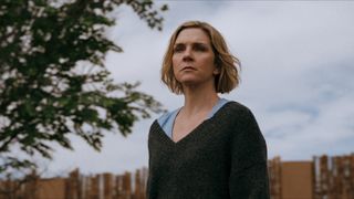 Rhea Seehorn as Carol standing in a yard in Pluribus.